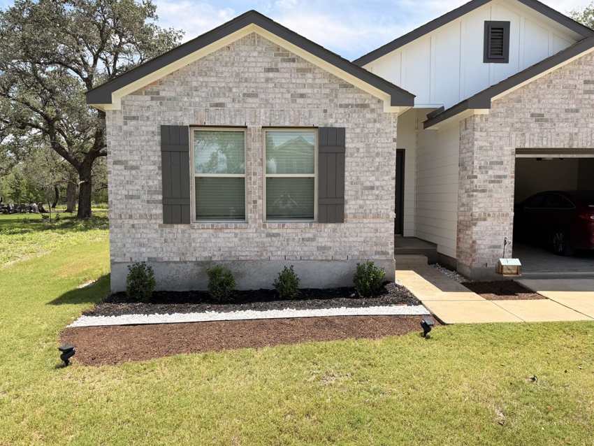 Finished front landscaping with mulch beds, white stone border, and shrubs