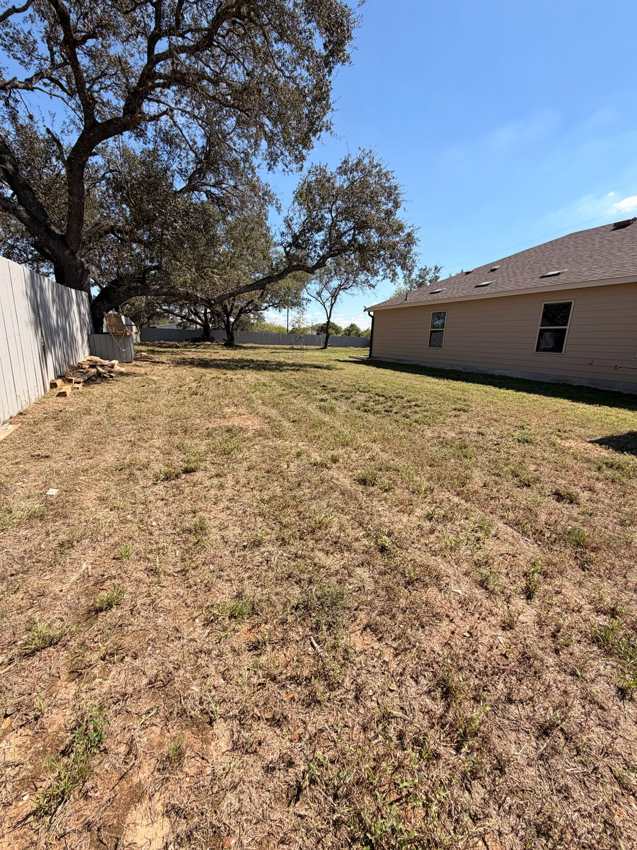 Open patchy yard beside a tan house before site prep